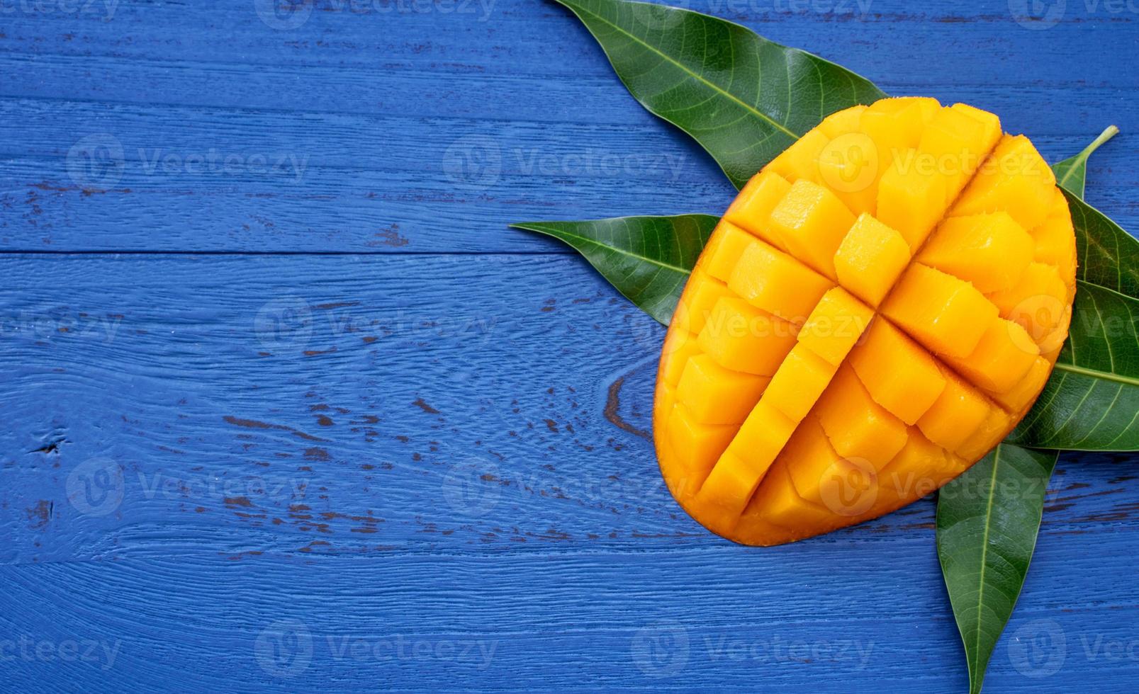 Fresh mango - beautiful chopped fruit with green leaves on dark blue timber background. Tropical fruit design concept. Flat lay. Top view. Copy space photo