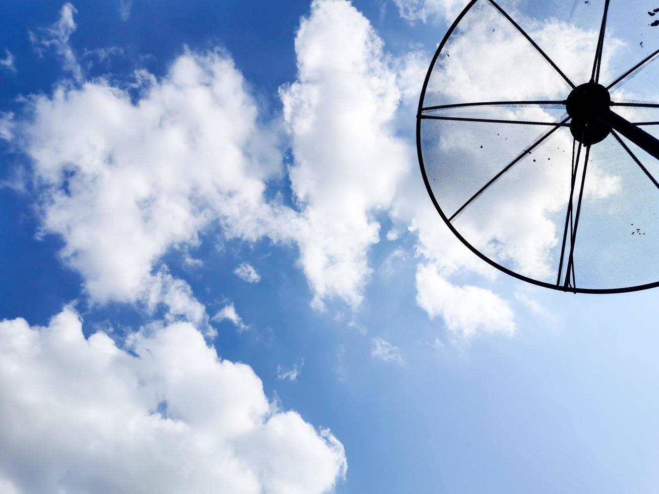 A picture of a cloudy daytime sky and a home TV satellite dish. photo