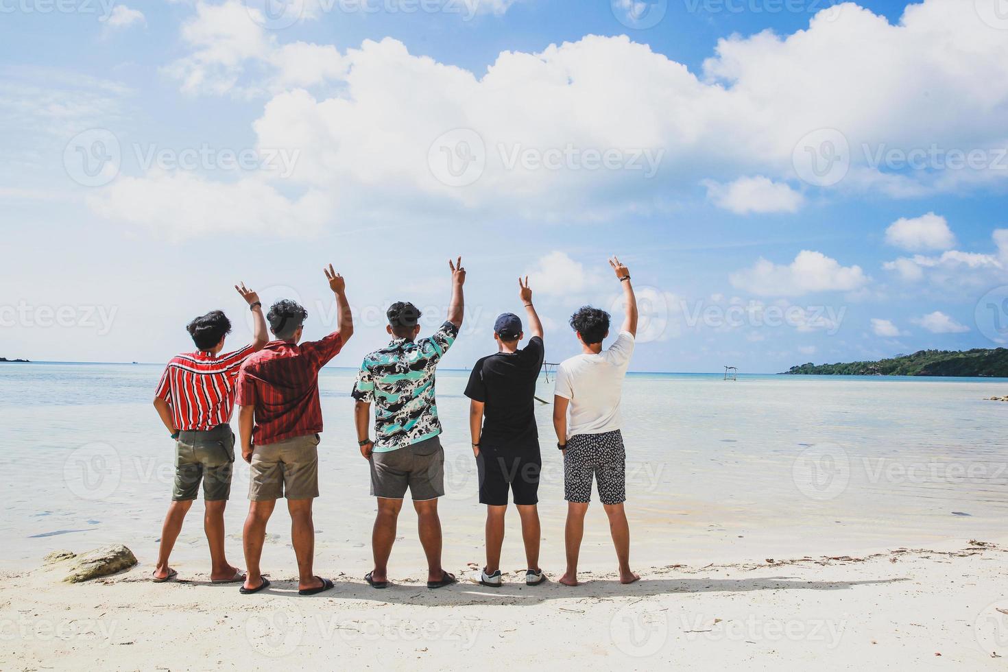 grupo de amigos de pie y levantando la mano juntos disfrutando de la vista de la playa tropical durante las vacaciones de verano foto