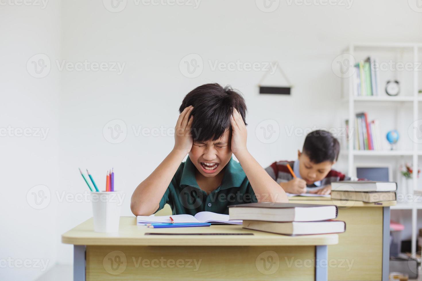 niño de escuela primaria cansado y estresado haciendo exámenes en clase foto