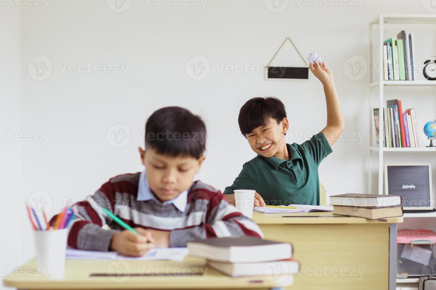 Naughty schoolboy pranks his friend who is studying with a paper ball photo