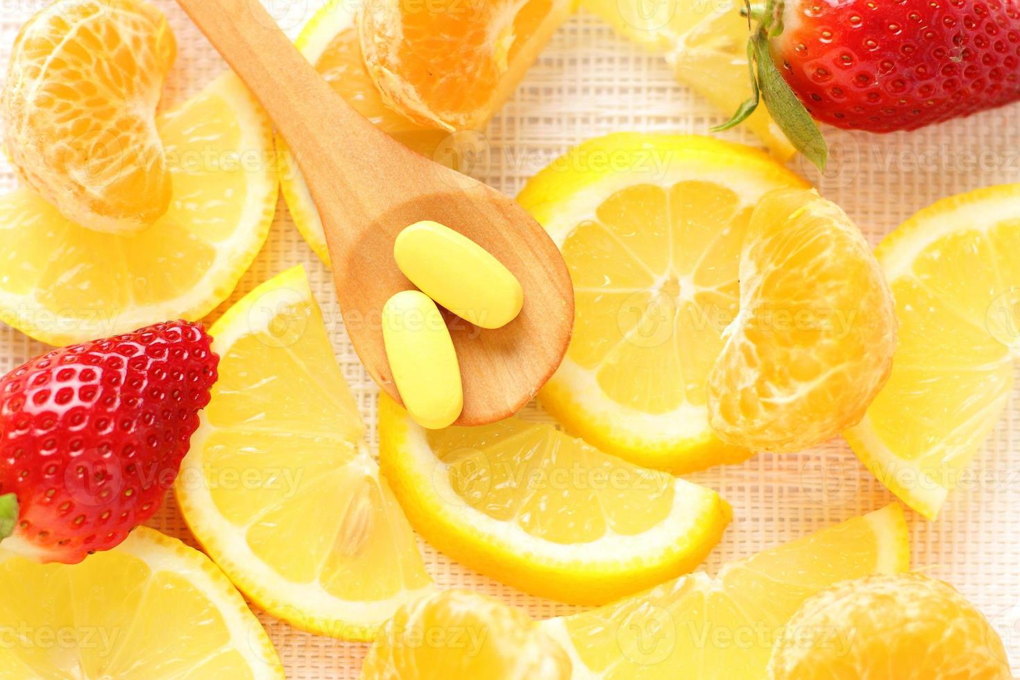 Vitamins pills on wooden spoon with lemon, orange, raspberry on background photo