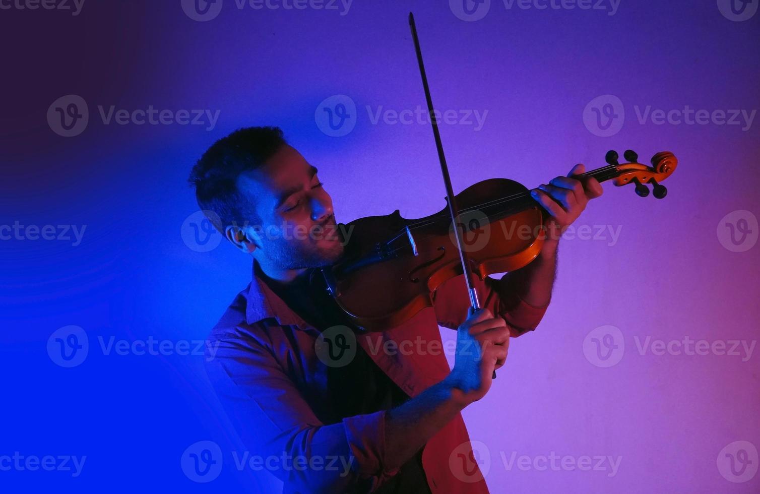 hombre tocando el violín en el estudio luces de neón con poca luz foto