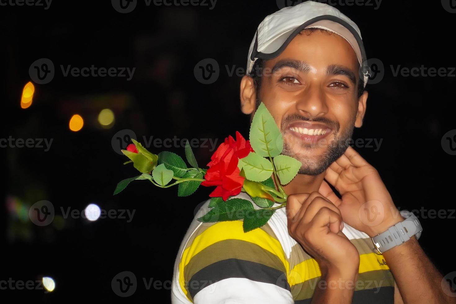 joven indio sonriendo feliz sosteniendo una flor de rosa en la noche foto