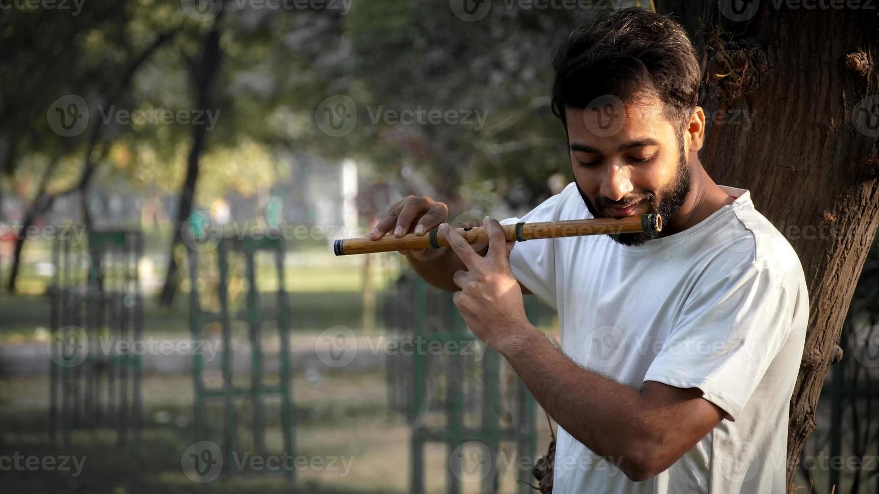 reproductor bansuri tocando música bajo el sol en el parque - flautista indio foto