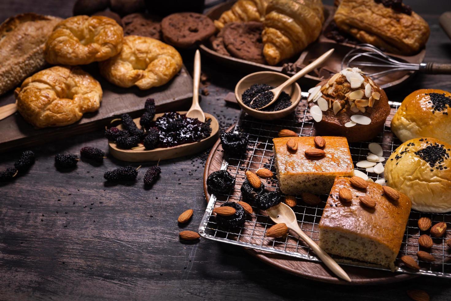 Various kinds of bakery and sweet bread with fresh mulberry and mulberry jam on wood table. Assortment of baked bread on dark wooden plate with copy space photo