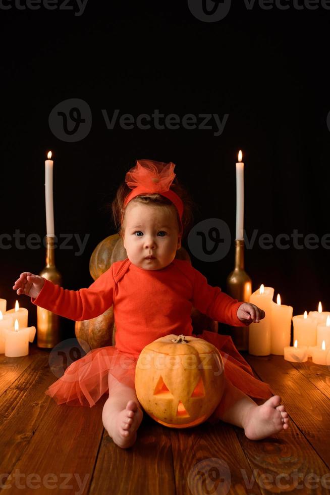 Little girl sits on a background of Jack pumpkins and candles on a black background. photo