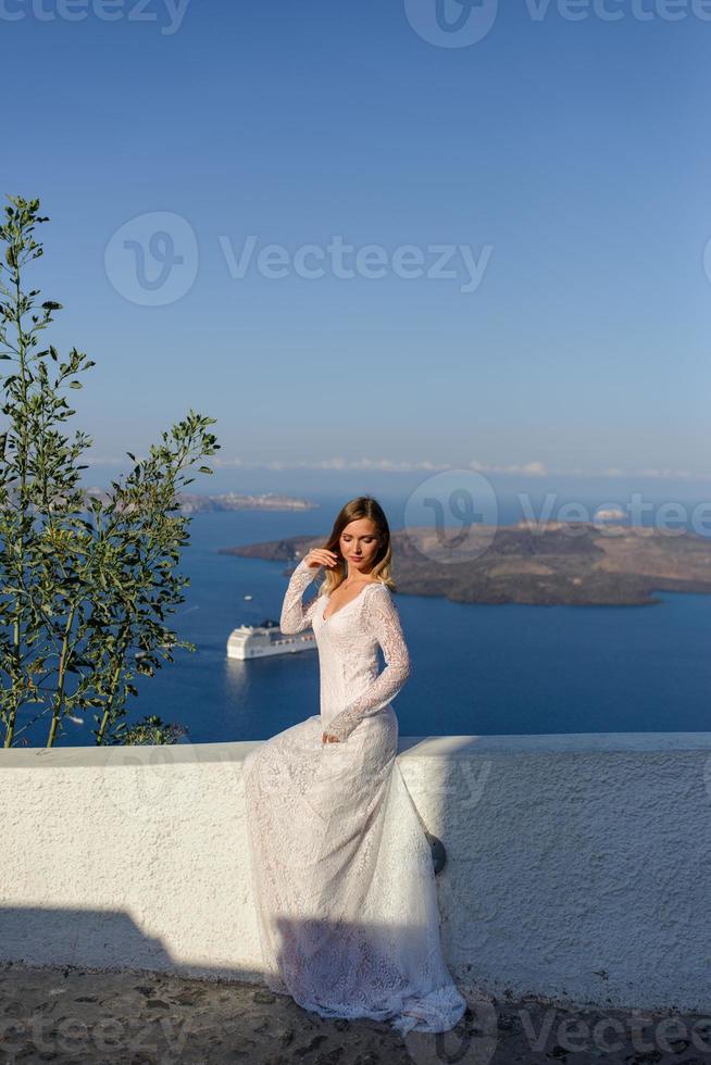 bella novia con un vestido blanco posando sobre el fondo del mar mediterráneo en thira, santorini. foto