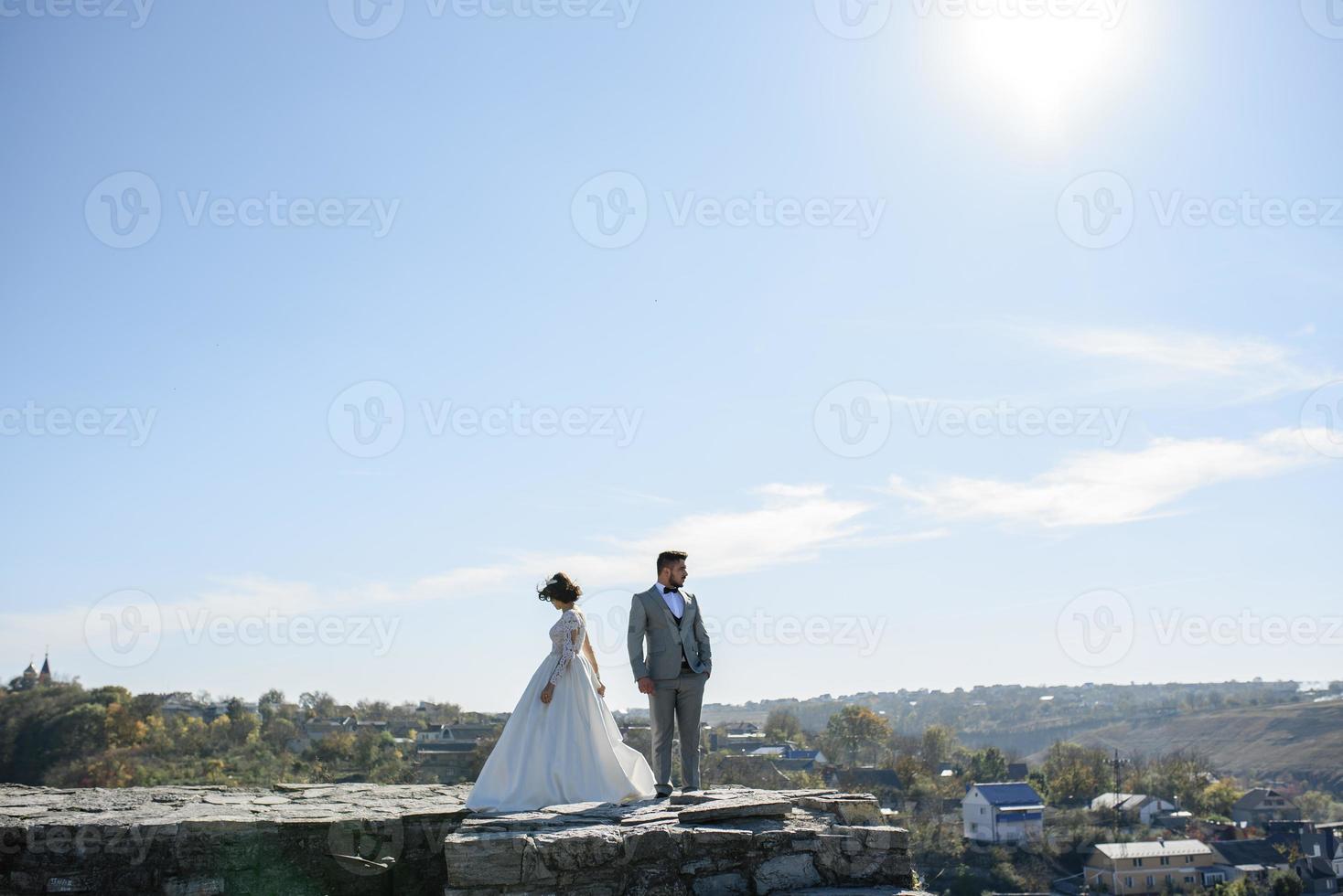 la novia y el novio caminan cerca del antiguo castillo. la pareja está de espaldas el uno al otro. foto