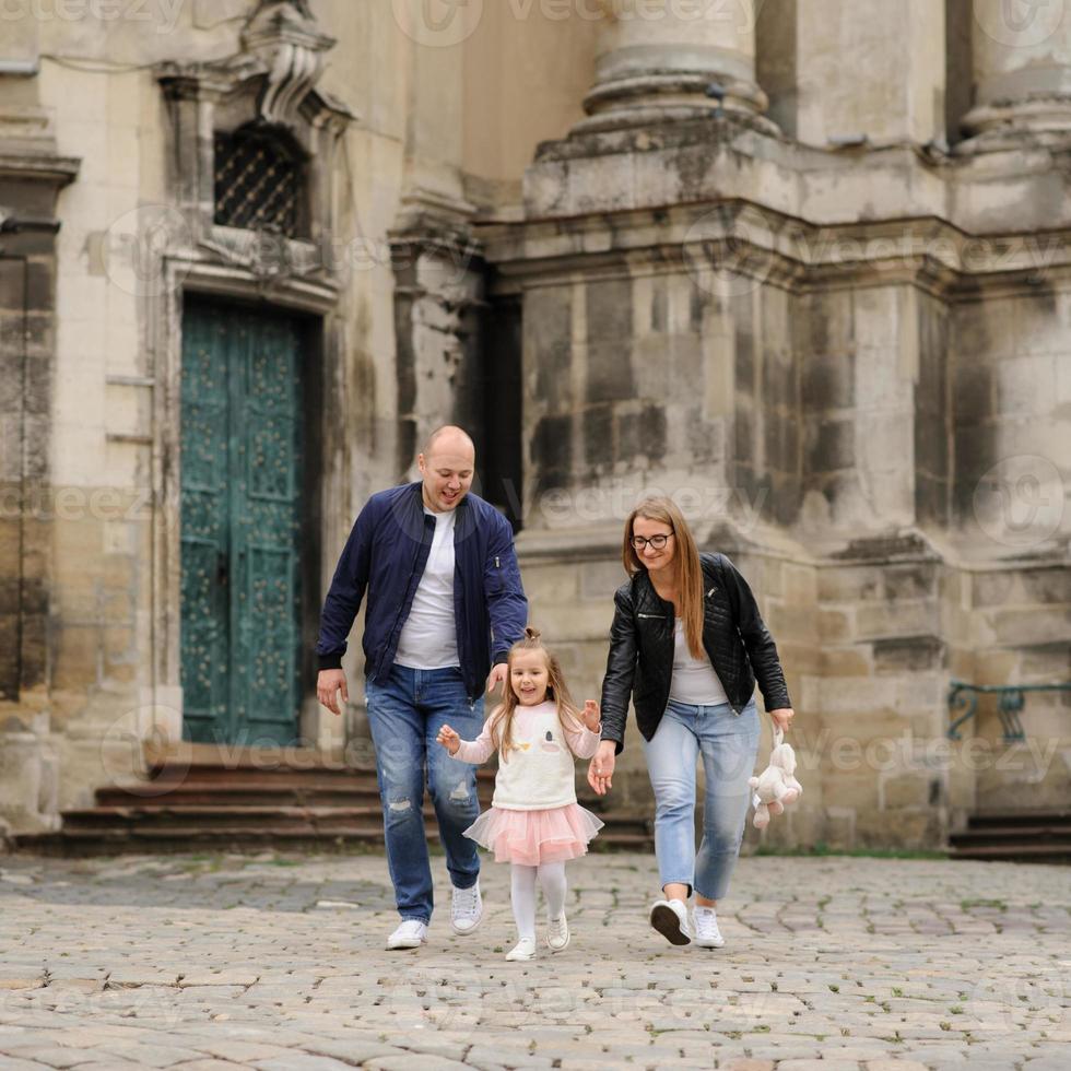 Parents and their daughter are sitting on the steps of an old church. photo