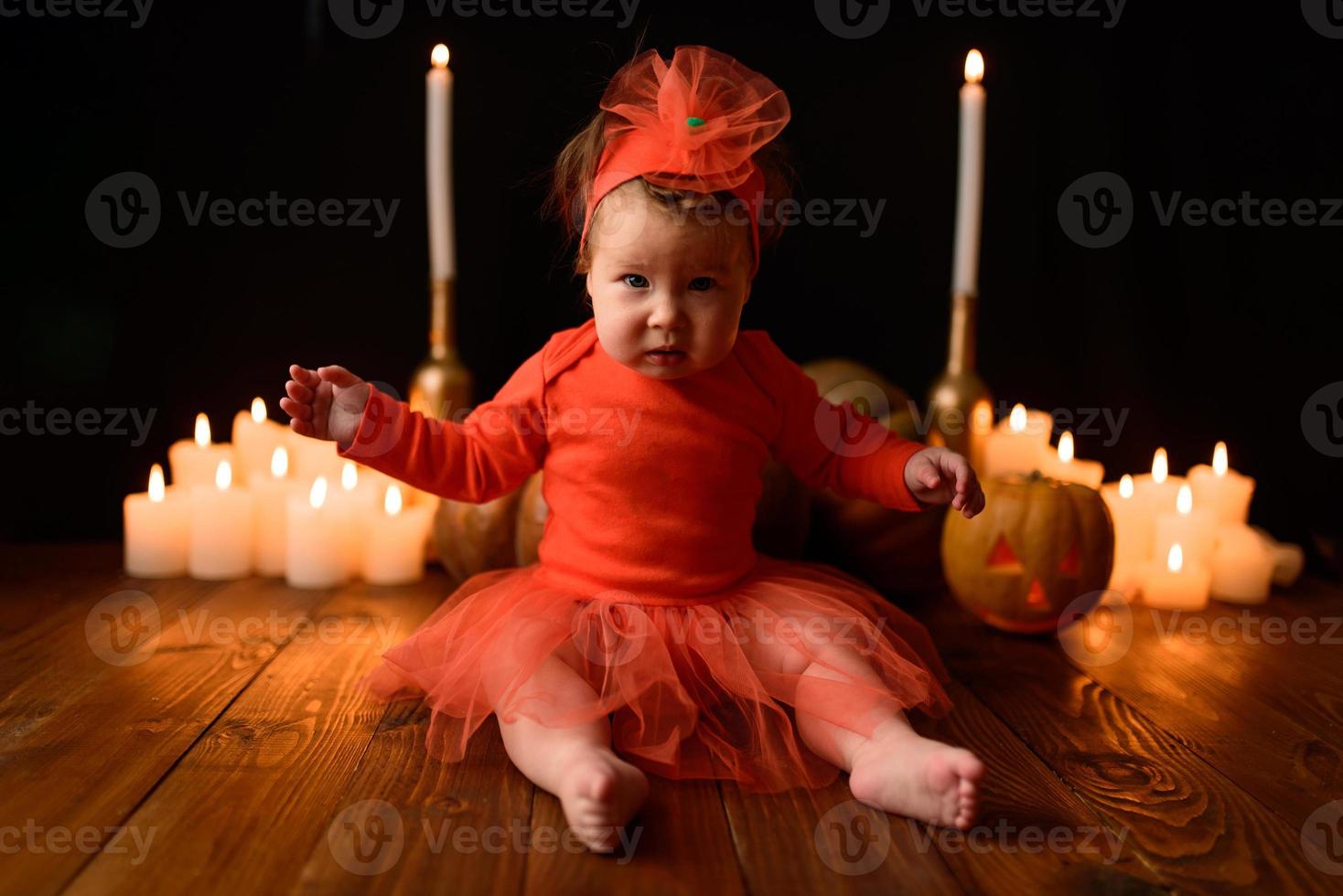 la niña se sienta sobre un fondo de calabazas y velas sobre un fondo negro. foto