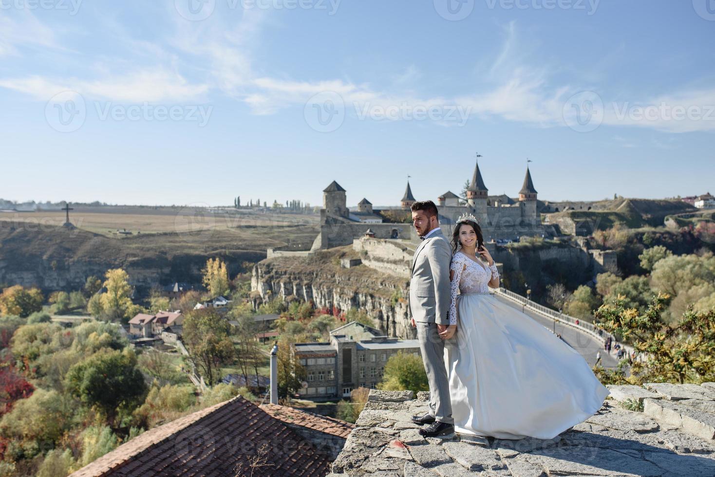 The bride and groom are walking near the old castle. The couple stands with their backs to each other. photo