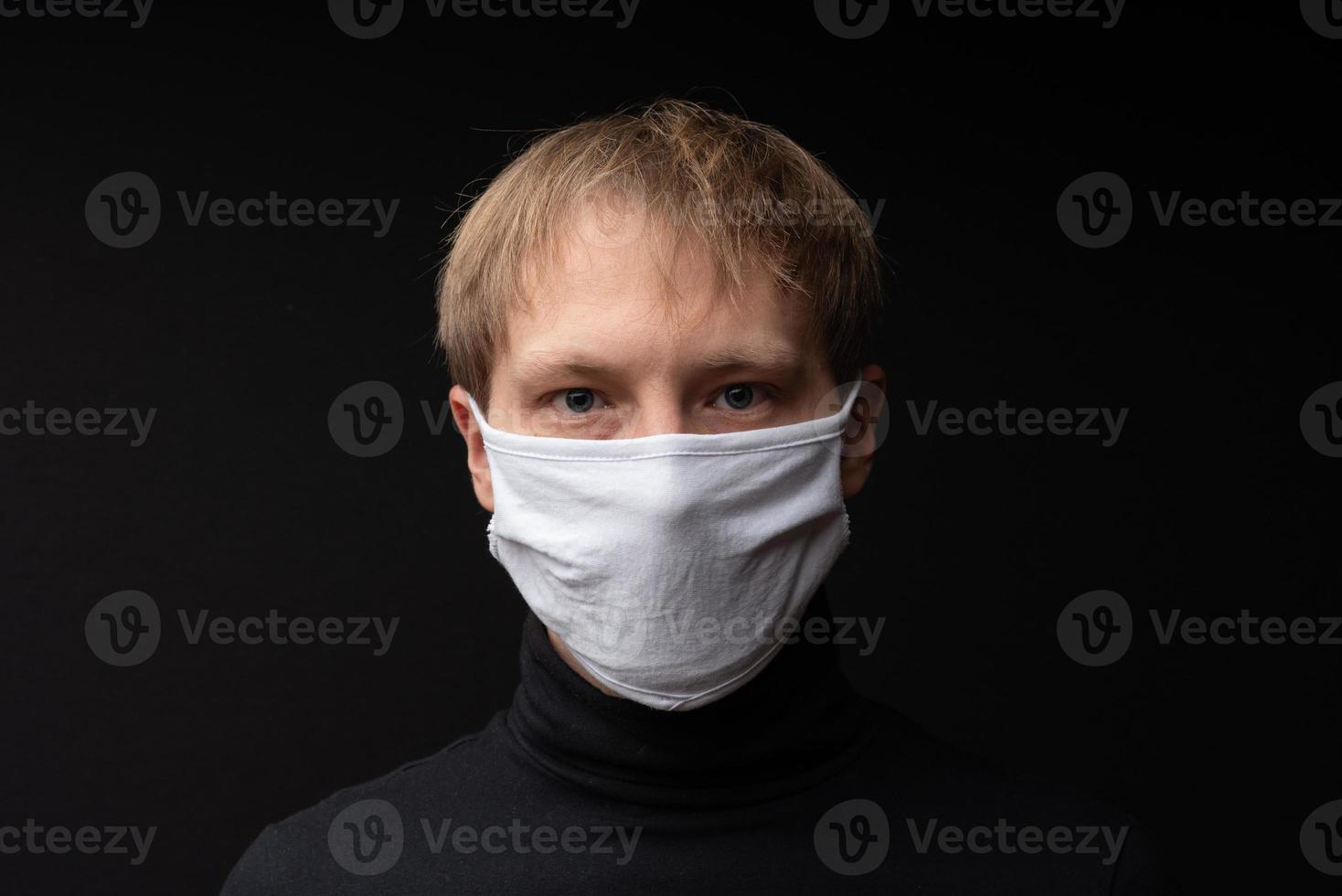 A man in a medical mask looks at the camera. Shot on a black background. photo