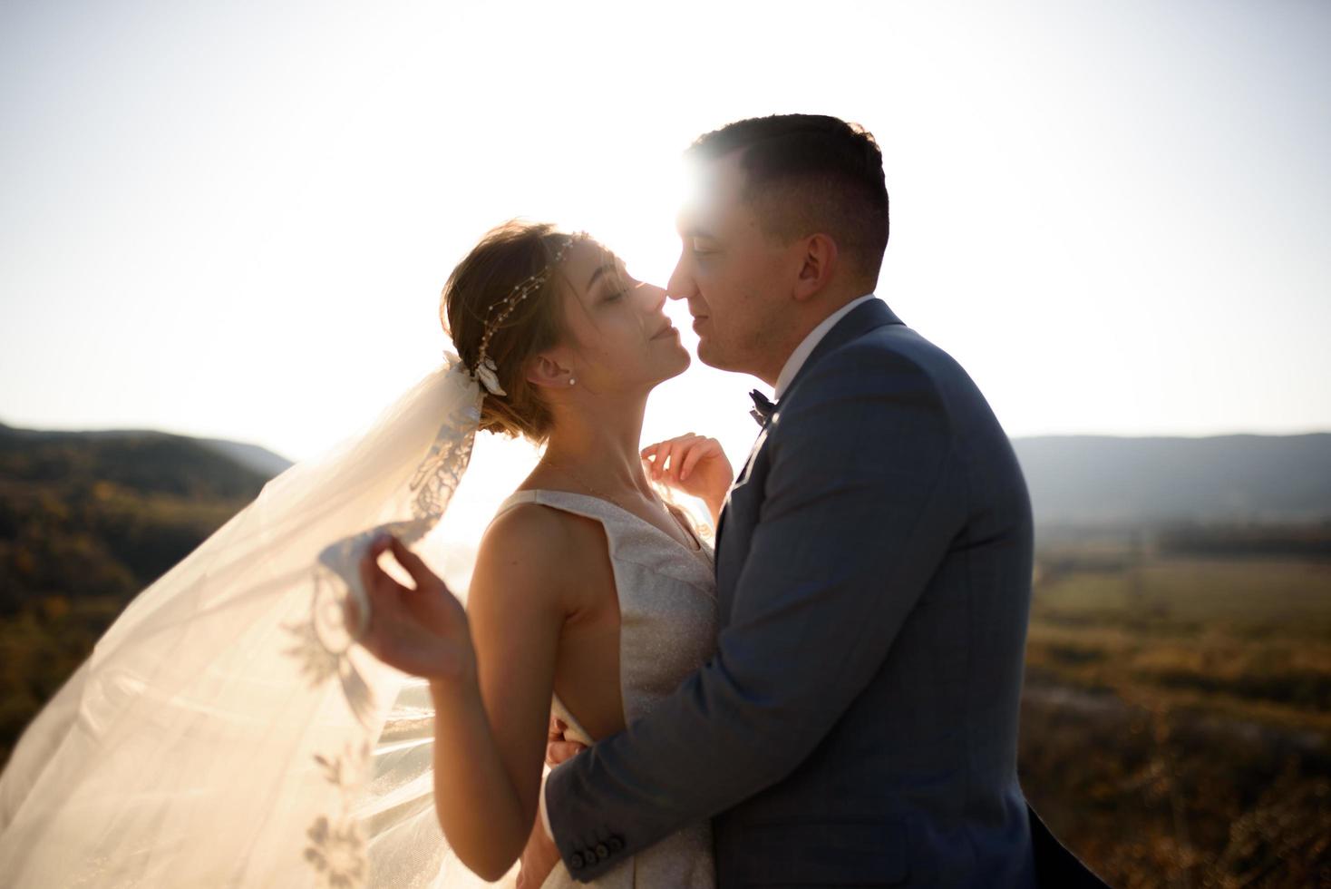 retrato de una joven novia hermosa y su marido en las montañas con un velo. el viento desarrolla un velo. fotografía de boda en la montaña. foto