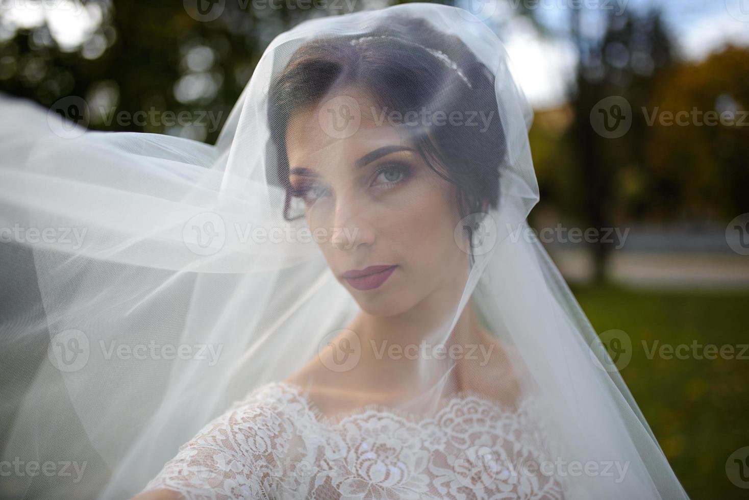 Portrait of a lonely bride on a background of an autumn park. The girl took refuge under a veil with which the wind develops. photo