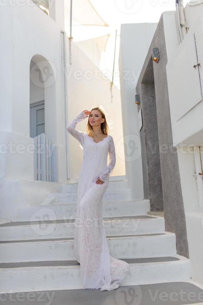 Portrait of a beautiful bride in a white dress. A girl poses on a background of white steps and white walls in Oia, Santorini. photo
