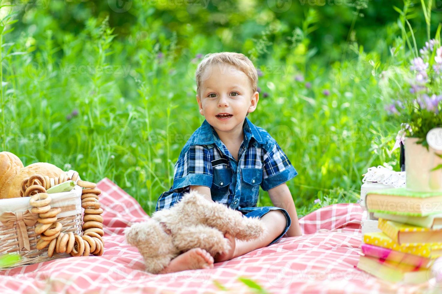 un niño lindo se sienta en una manta y juega con su oso de peluche. foto