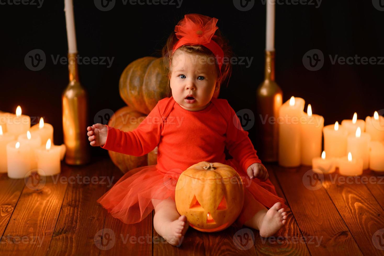 Little girl sits on a background of Jack pumpkins and candles on a black background. photo