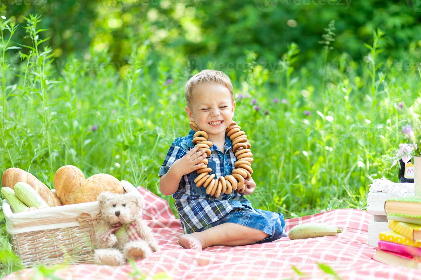 un niño lindo se sienta en una manta y se divierte en verano en la naturaleza. en el cuello de los niños hay un collar de bagel. foto