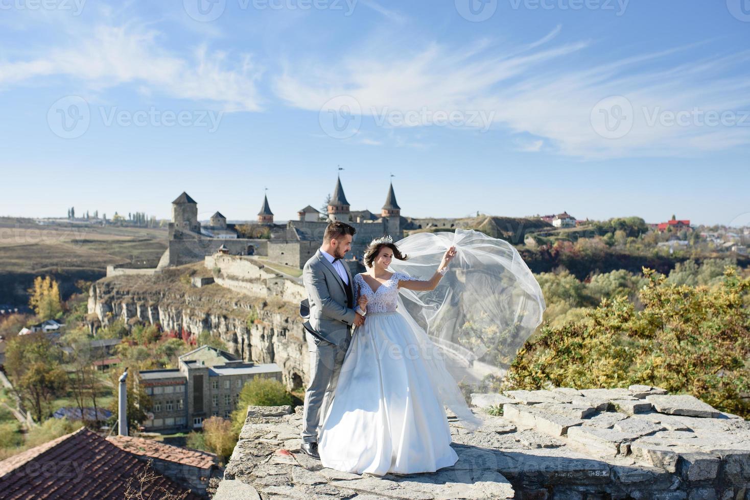 The bride and groom are walking near the old castle. The couple stands with their backs to each other. photo