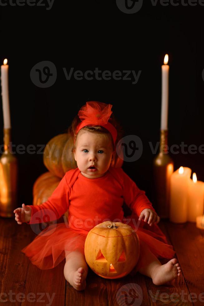 Little girl sits on a background of Jack pumpkins and candles on a black background. photo