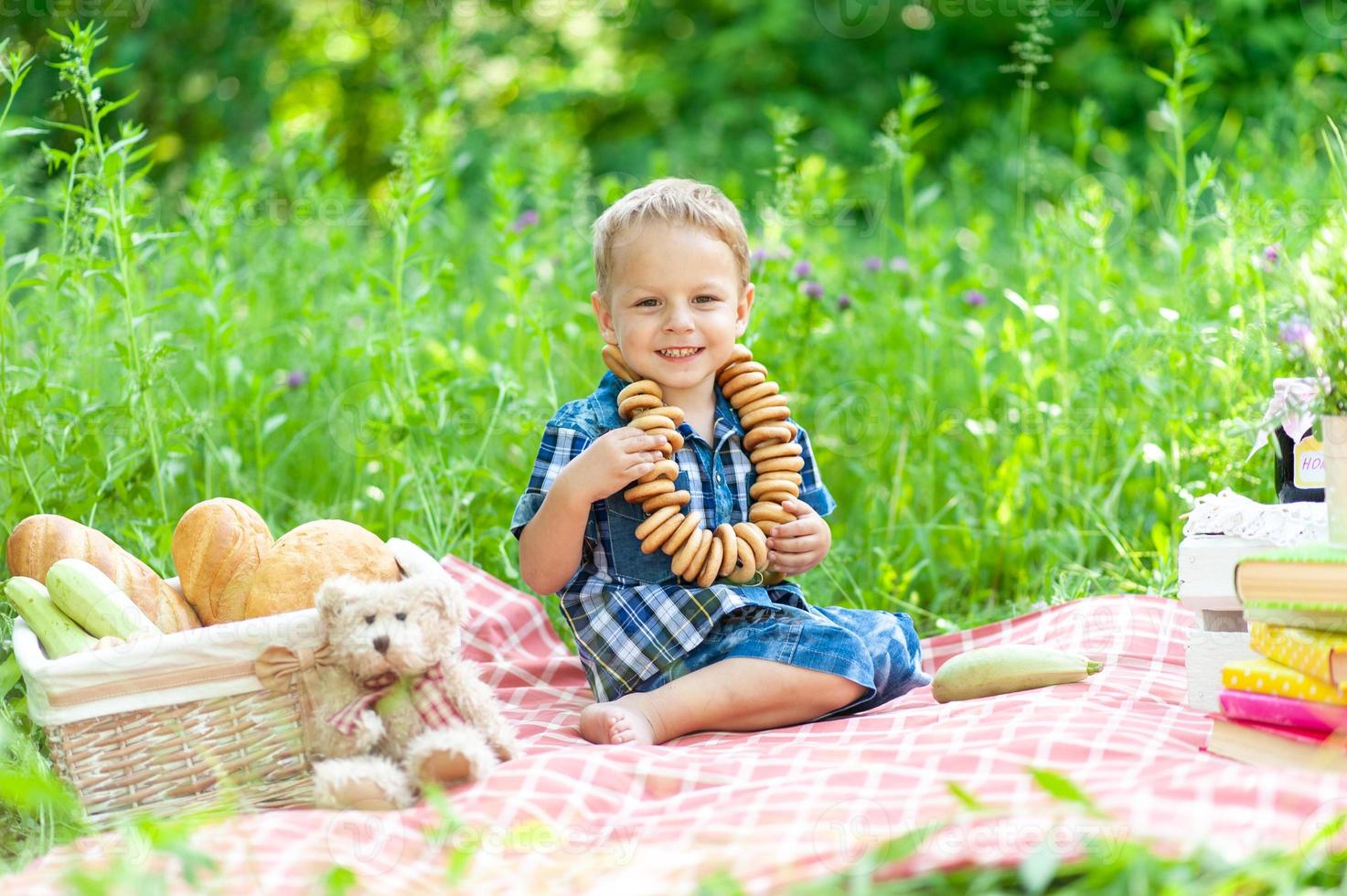 Little cute boy sits on a plaid and has fun summertime in nature. On the boys neck is a bagel necklace. photo