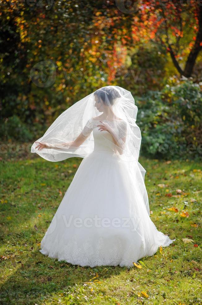 Portrait of a lonely bride on a background of an autumn park. The girl took refuge under a veil with which the wind develops. photo
