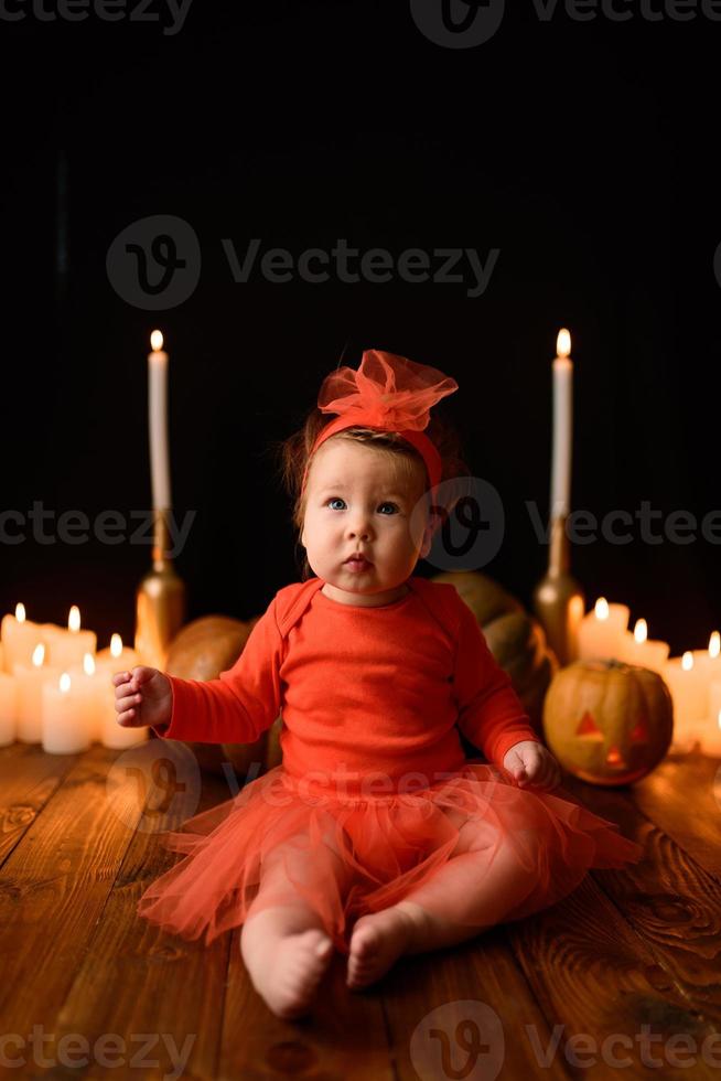 Little girl sits on a background of Jack pumpkins and candles on a black background. photo