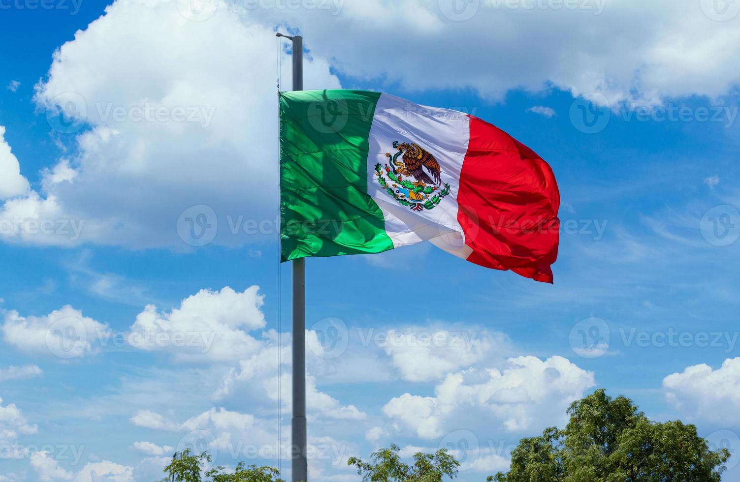 los cabos, méxico, bandera tricolor mexicana a rayas ondeando orgullosamente en el mástil en el aire con el símbolo azteca de tenochtitlan foto