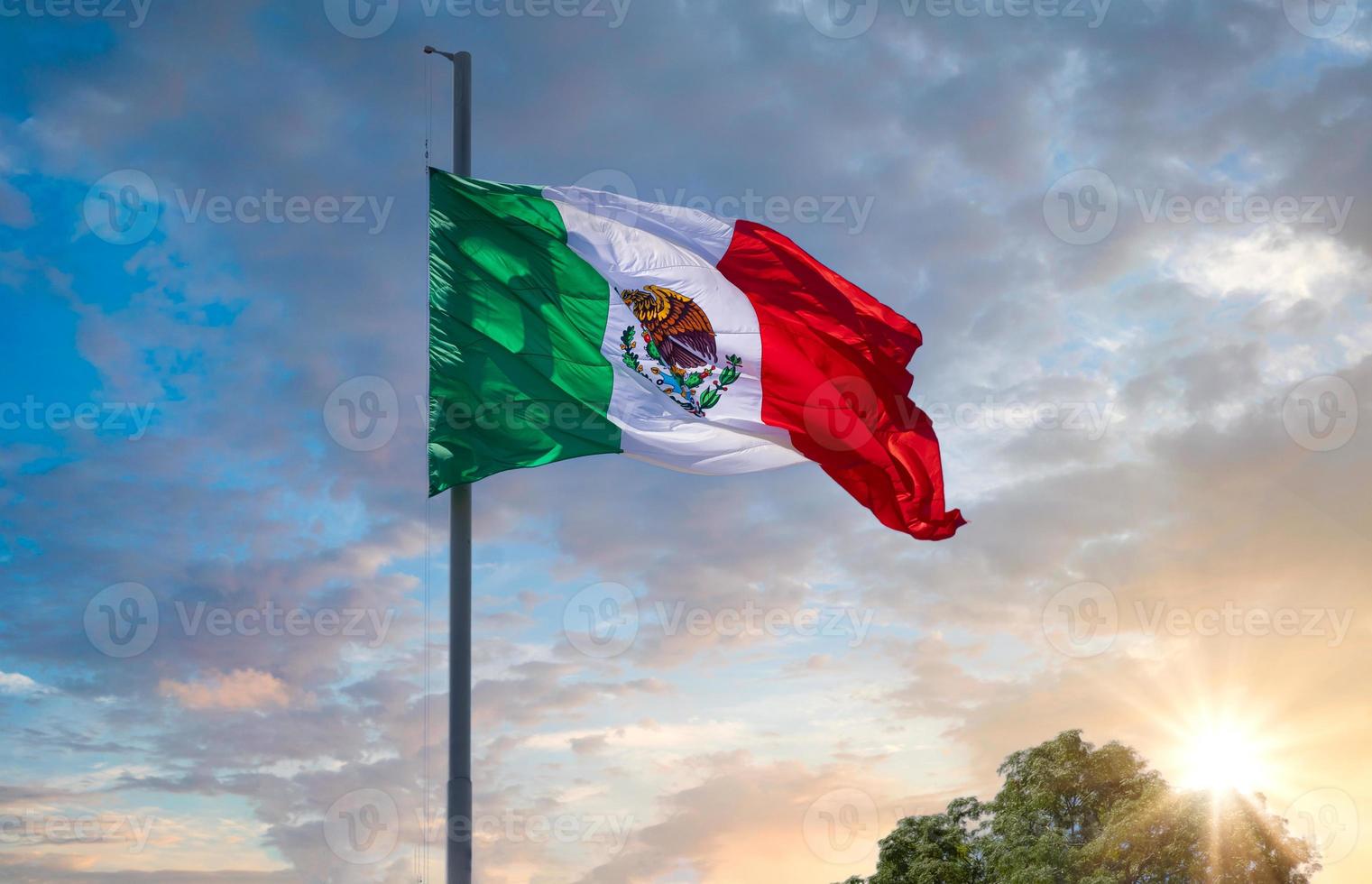 los cabos, méxico, bandera tricolor mexicana a rayas ondeando orgullosamente en el mástil en el aire con el símbolo azteca de tenochtitlan foto