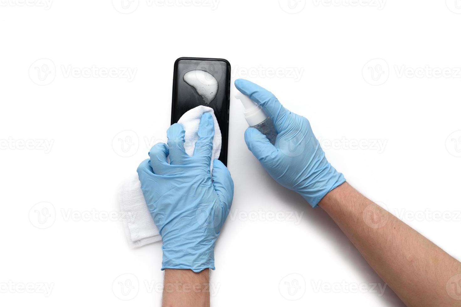 las manos masculinas con guantes médicos tratan el teléfono con un antiséptico para no contraer coronavirus. Aislado en un fondo blanco. foto