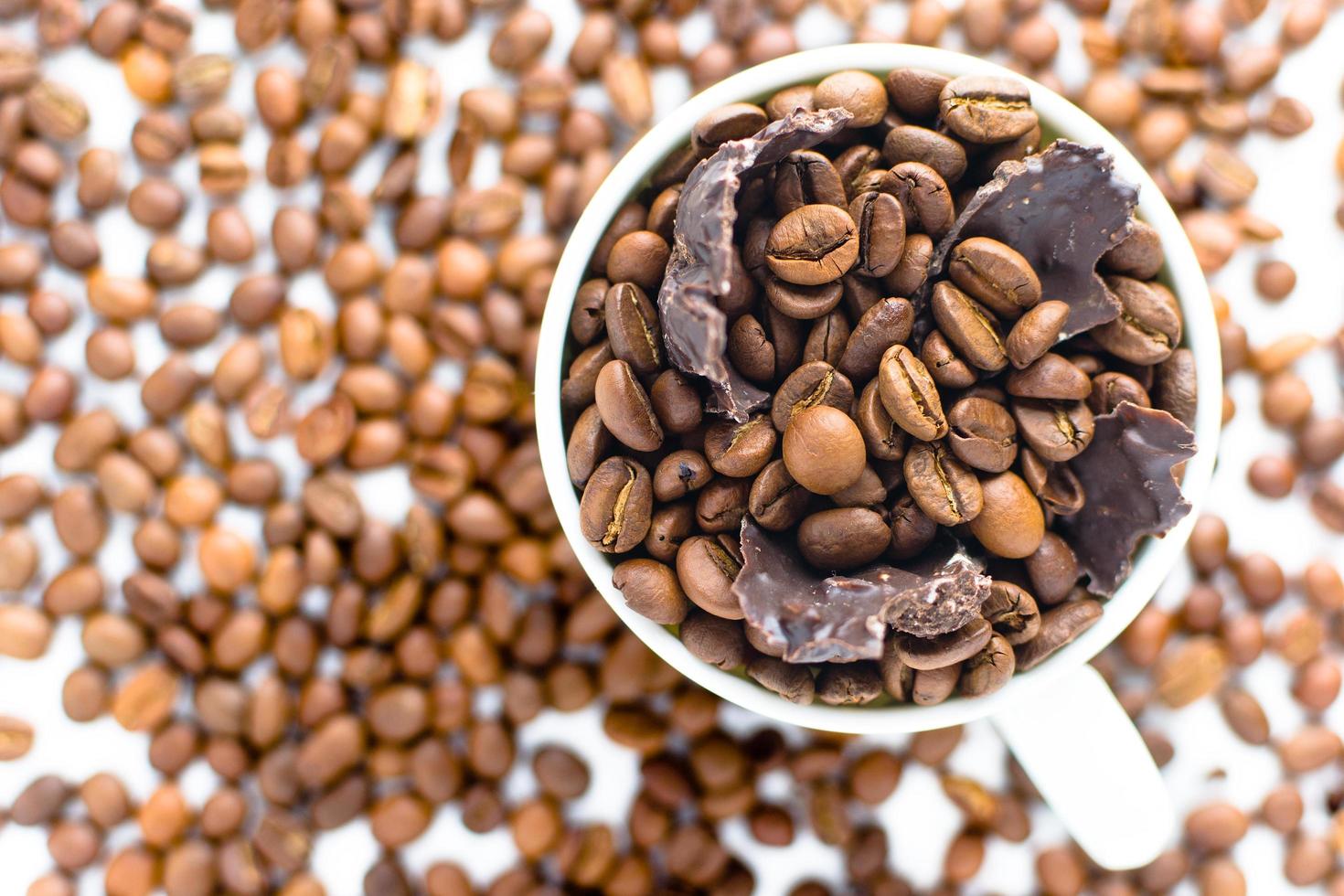 taza blanca con granos de café y trozos de chocolate negro sobre un mantel blanco foto