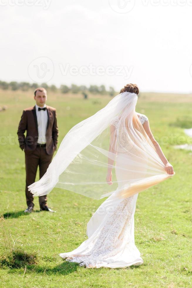 una hermosa novia se juega con su velo y está de espaldas a la cámara. el viento sopla un velo. centrarse en la novia. foto