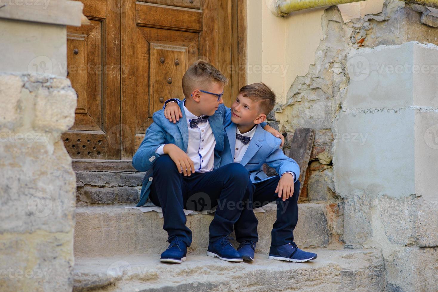 Two little boys, brothers are dressed in a suit. Children are standing in the park and hugging. photo