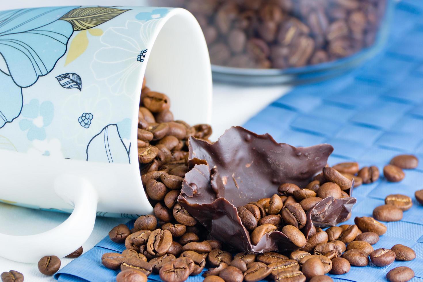 taza blanca con granos de café y trozos de chocolate negro sobre un mantel blanco foto