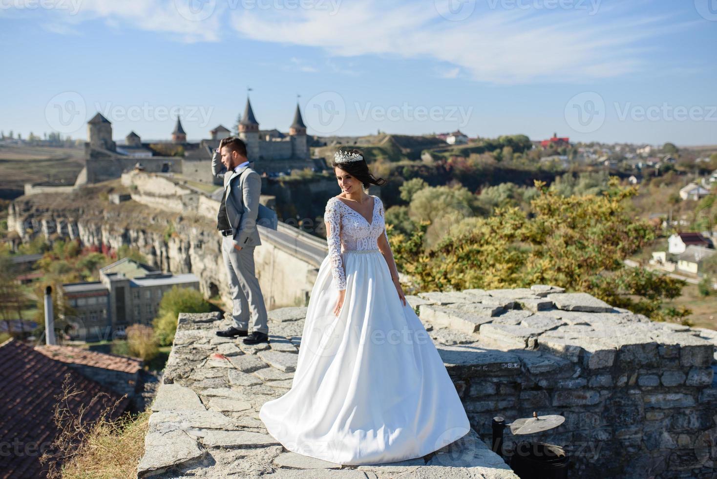 la novia y el novio caminan cerca del antiguo castillo. la pareja está de espaldas el uno al otro. foto