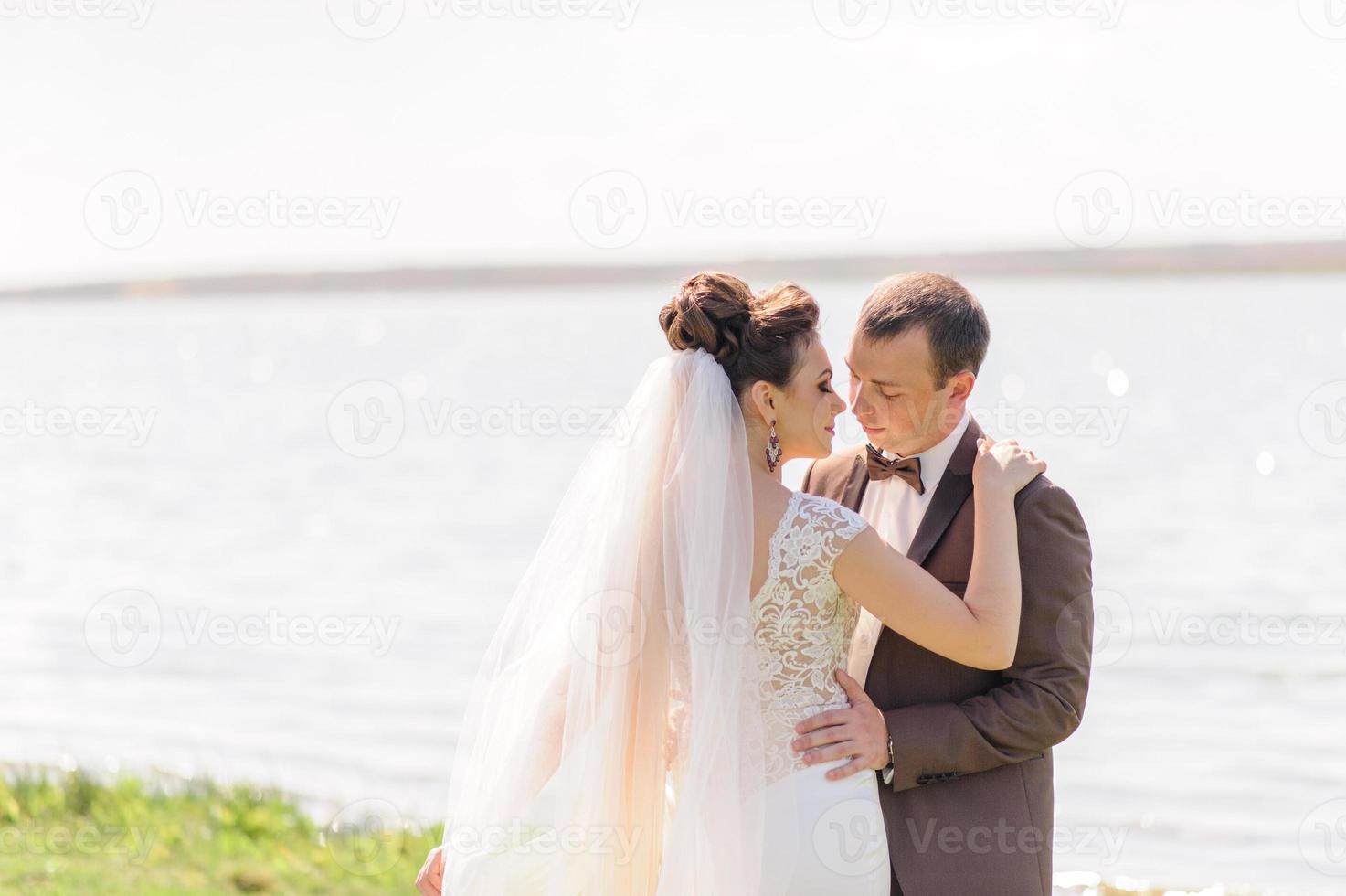 la novia y el novio se abrazan cerca del estanque en la naturaleza. el viento levanta un ligero velo. foto