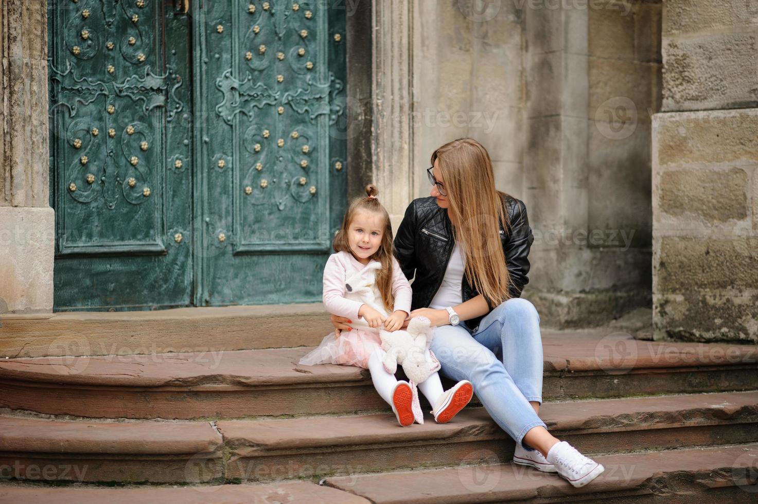 Parents and their daughter are sitting on the steps of an old church. photo