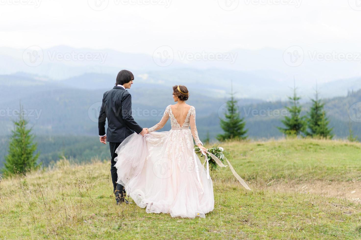 la novia y el novio caminan de la mano contra el fondo de las montañas. Fotografía de boda. foto
