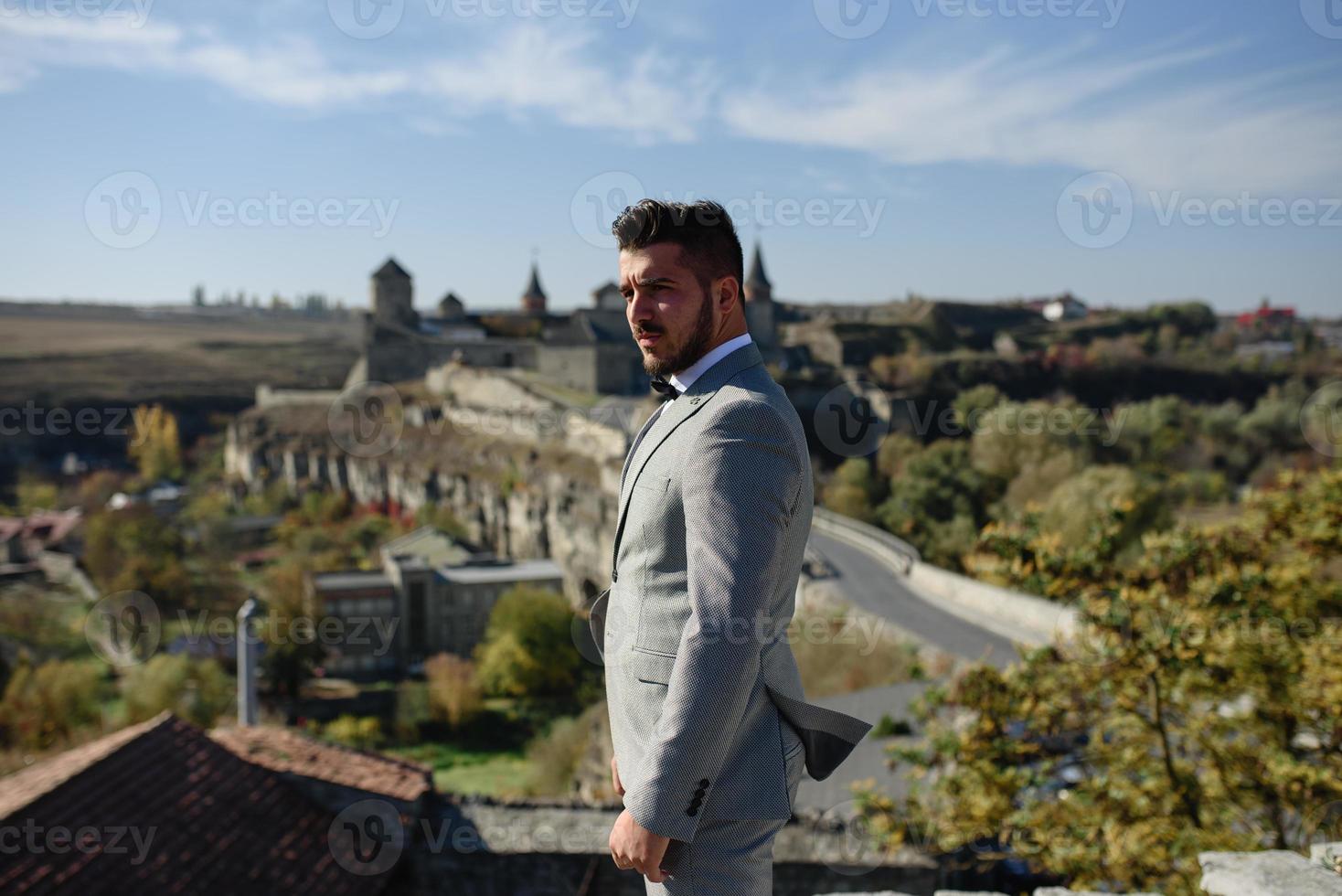 The bride and groom are walking near the old castle. The couple stands with their backs to each other. photo