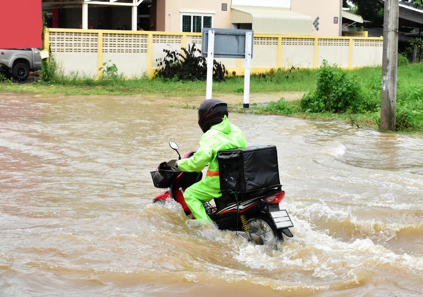 Delivery Asian man wearing green uniform, riding and delivering food to customer with food case box behind in flood street, express food delivery and shopping online concept in the flood situation . photo