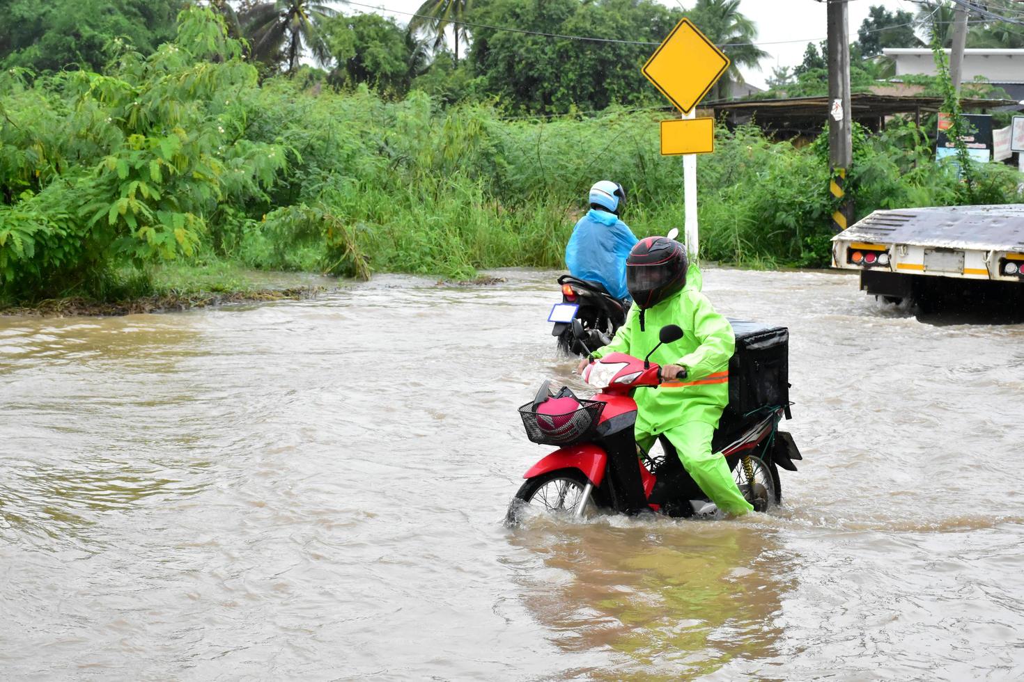 Delivery Asian man wearing green uniform, riding and delivering food to customer with food case box behind in flood street, express food delivery and shopping online concept in the flood situation . photo