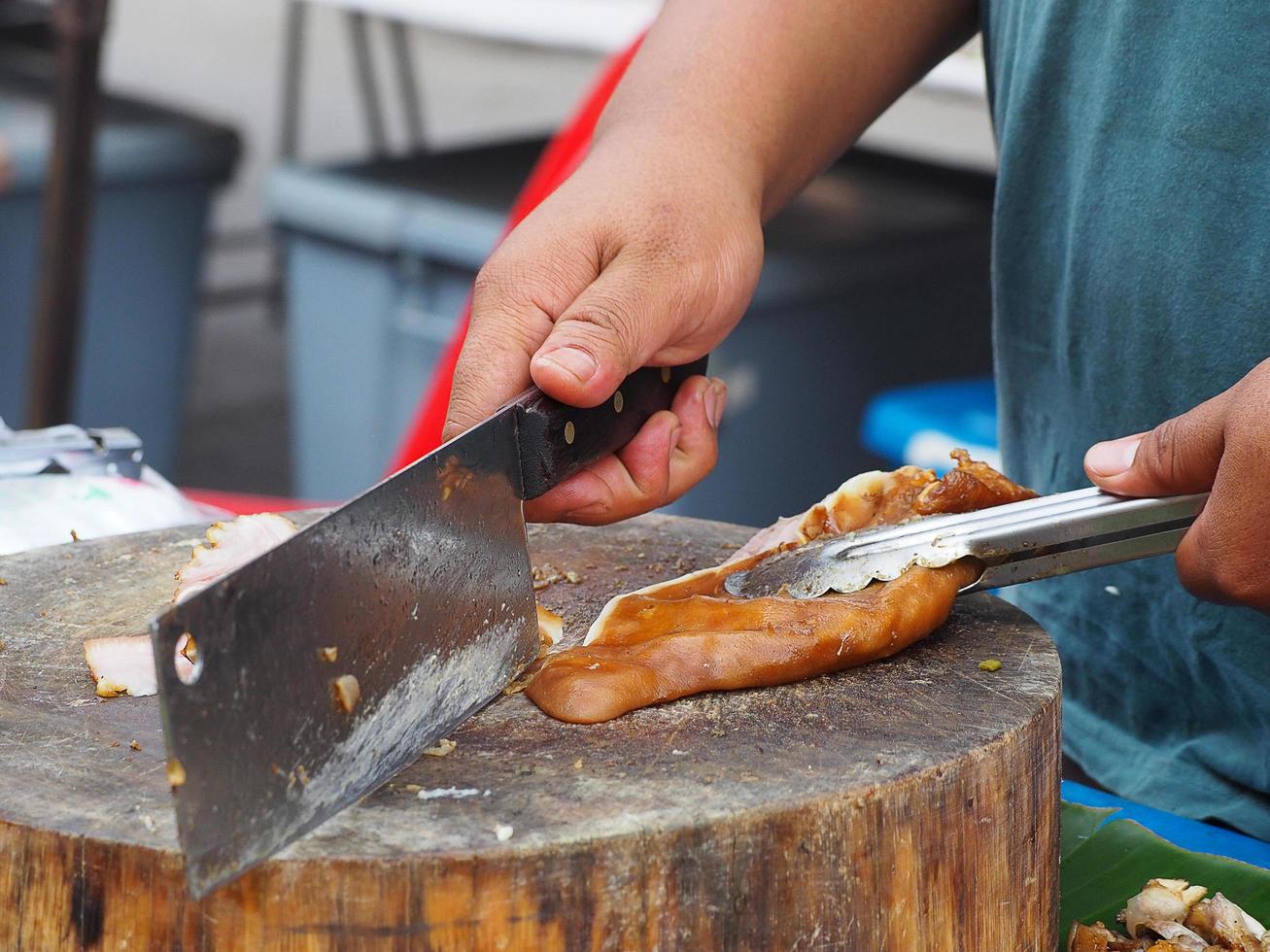 joven sosteniendo un cuchillo cortando la oreja de cerdo guisada en una tabla de cortar foto