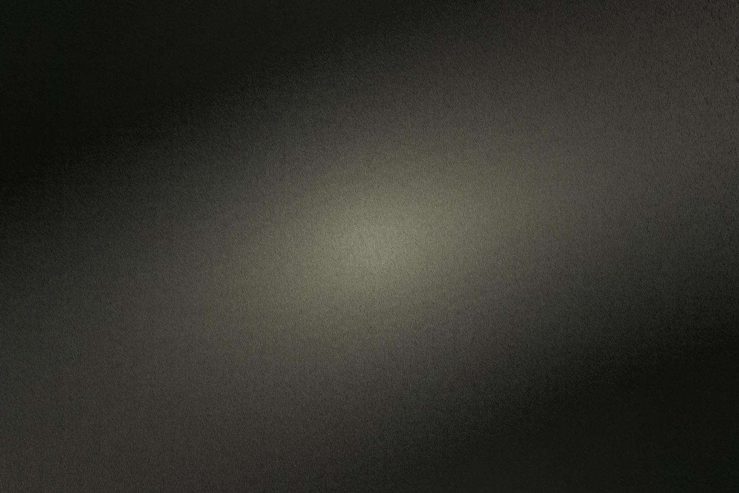 Black rough metal wall with light shining through in dark room, abstract background photo