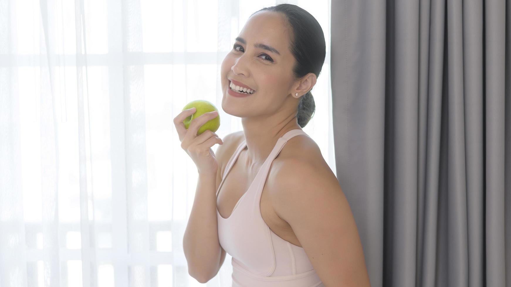 Fit young woman eating an apple after work out at home, sport and healthy lifestyle concept. photo