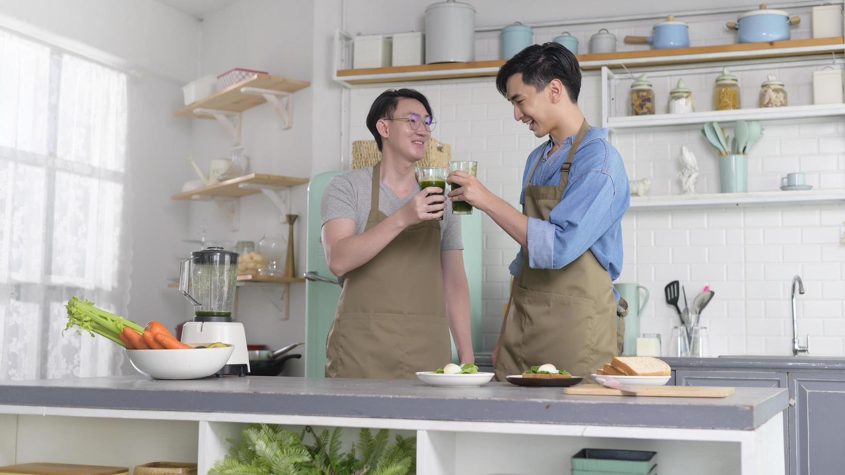 joven pareja gay sonriente haciendo jugo saludable con máquina de jugo en la cocina en casa, lgbtq y concepto de diversidad. foto
