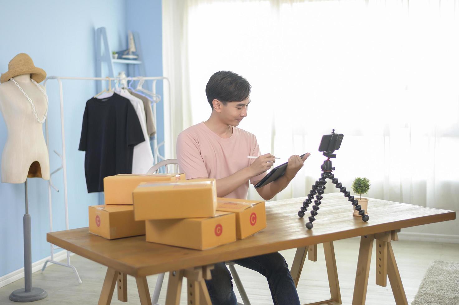 An Asian man is showing clothes in front of smartphone  live streaming at his shop. Technology online business concept. photo
