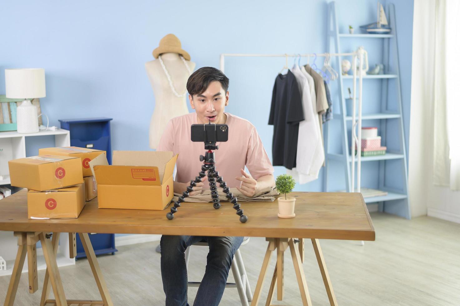 un hombre asiático está mostrando ropa frente a la transmisión en vivo de un teléfono inteligente en su tienda. concepto de negocio en línea de tecnología. foto