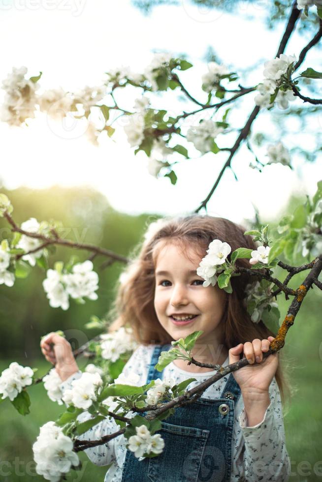 una linda niña de 5 años en un floreciente huerto de manzanas blancas en primavera. primavera, huerta, floración, alergia, fragancia primaveral, ternura, cuidado de la naturaleza. retrato foto