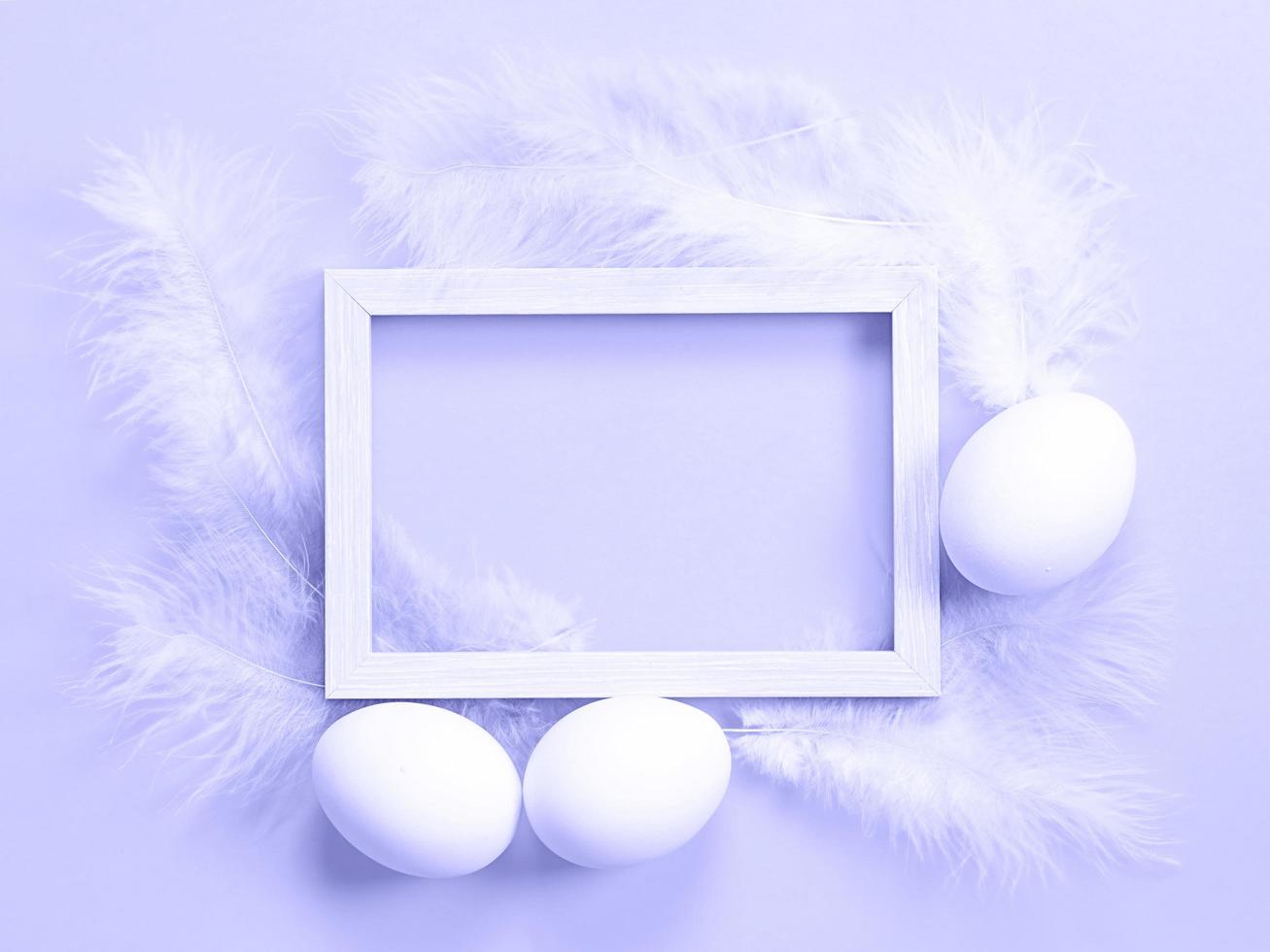Easter white frame on purple background very peri tinting of chicken eggs and colored delicate feathers. Spring, religious holiday, Easter decoration, greeting, copy space, mock up photo